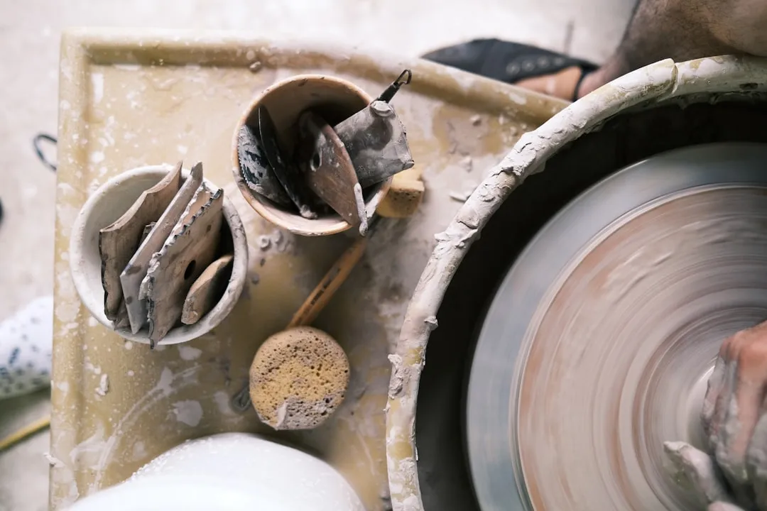 A person shaping clay on a spinning pottery wheel with tools in nearby bowls